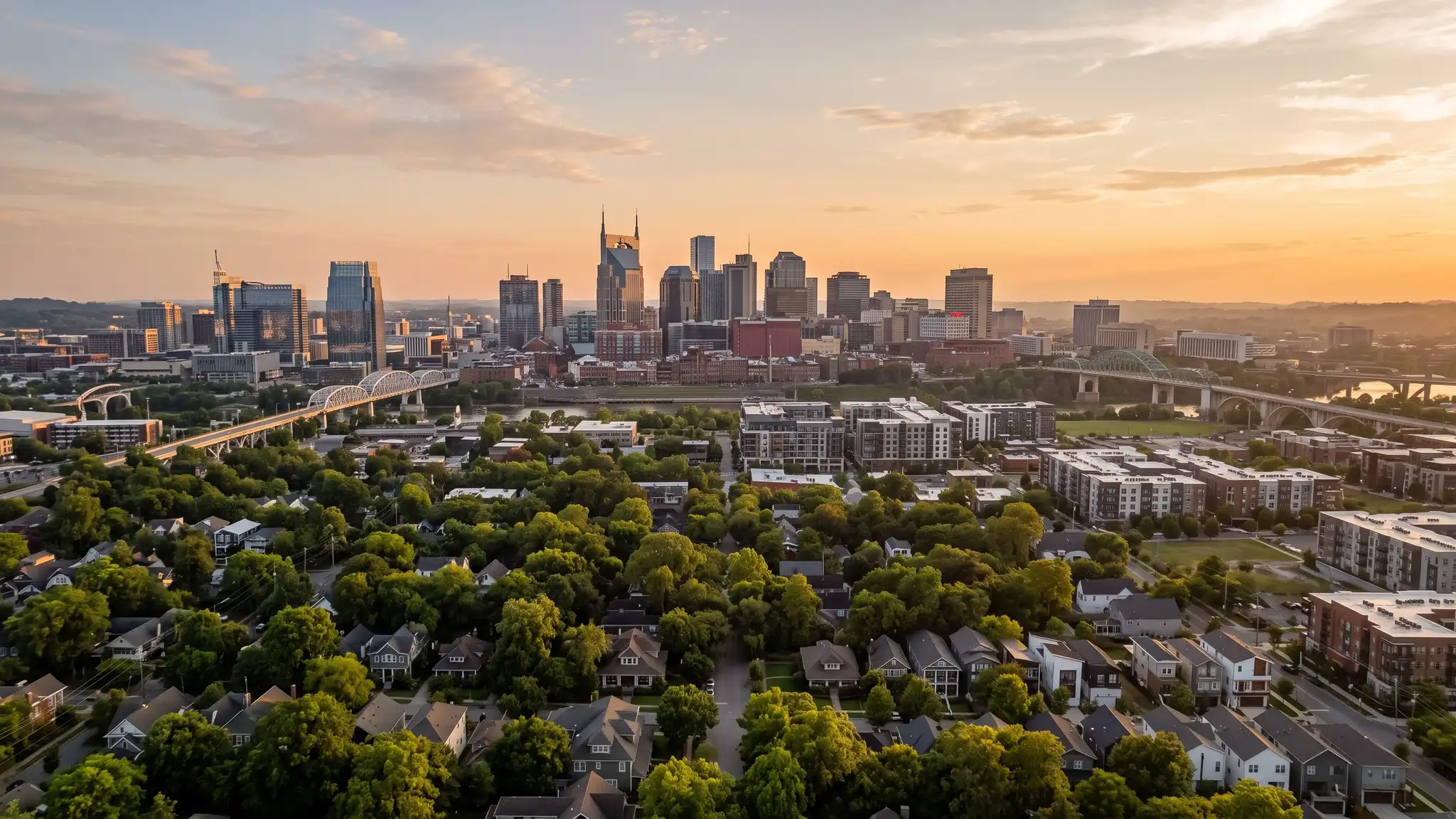 A golden hour view of the Nashville skyline with new modern buildings and tree-lined neighborhoods in the foreground